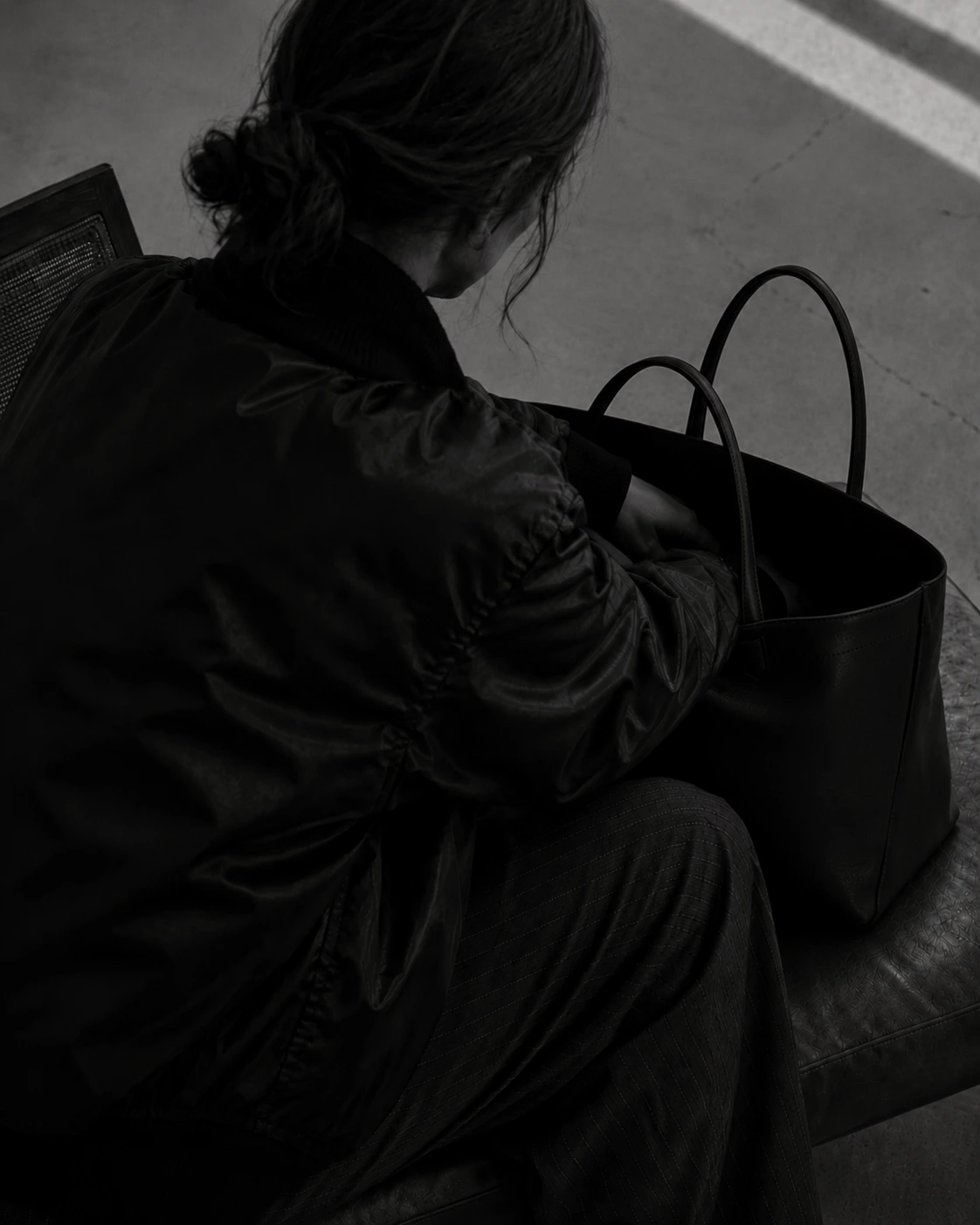 Editorial — a figure seated with a structured tote, in monochrome